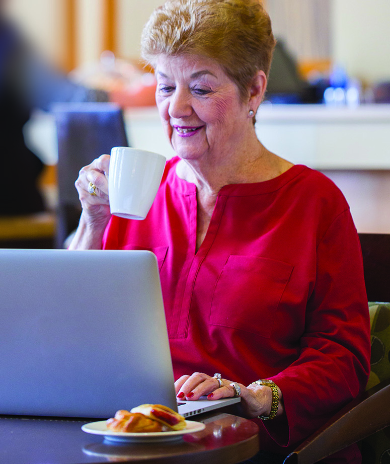 senior woman sitting at laptop drinking from a mug