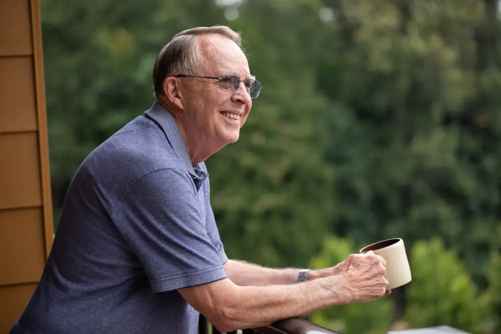a senior man looking over his balcony while enjoying his morning coffee