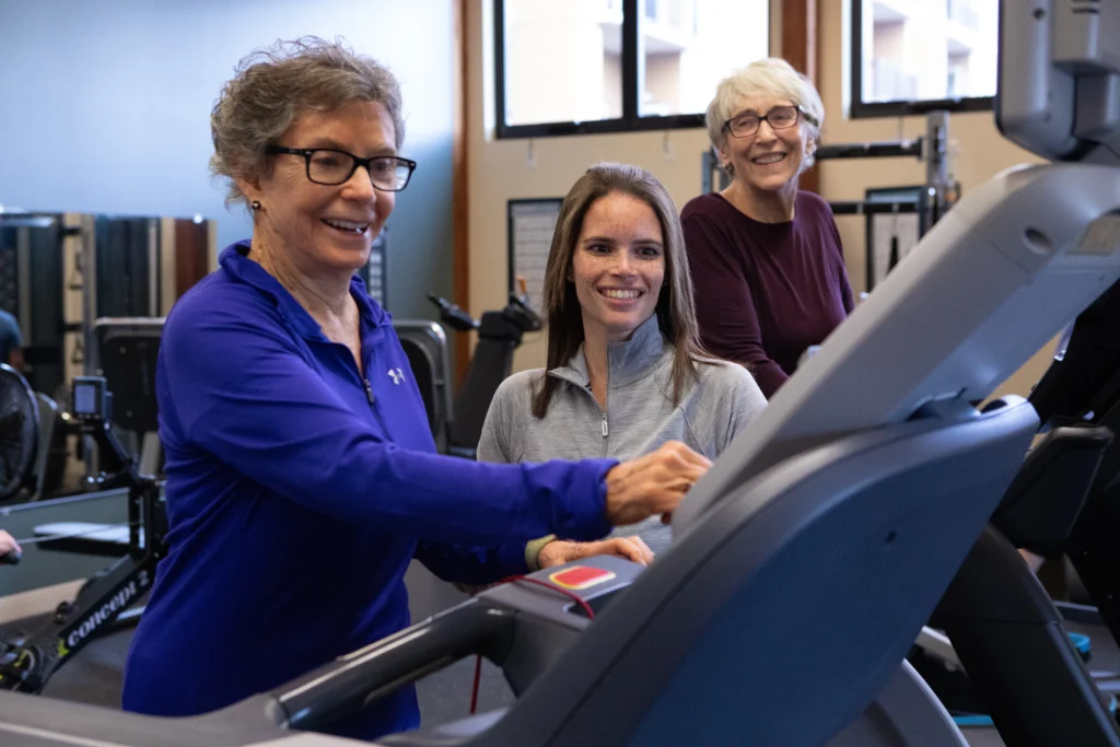 senior women at Timber Ridge at Talus working out with trainer on a treadmill and experiencing the luxury senior living amenities.