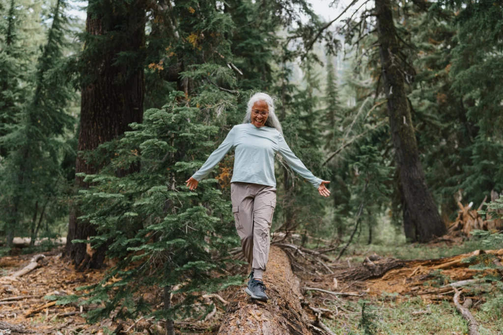 senior woman walking on log, taking advantage of the mental health benefits of nature for seniors in Issaquah, WA.